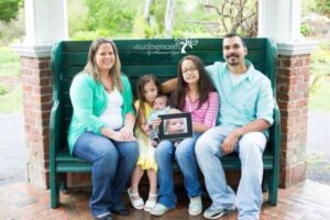 Picture of VYF advocate, Kathryn, and her family sitting on a bench, holding a picture of her late son, Brady